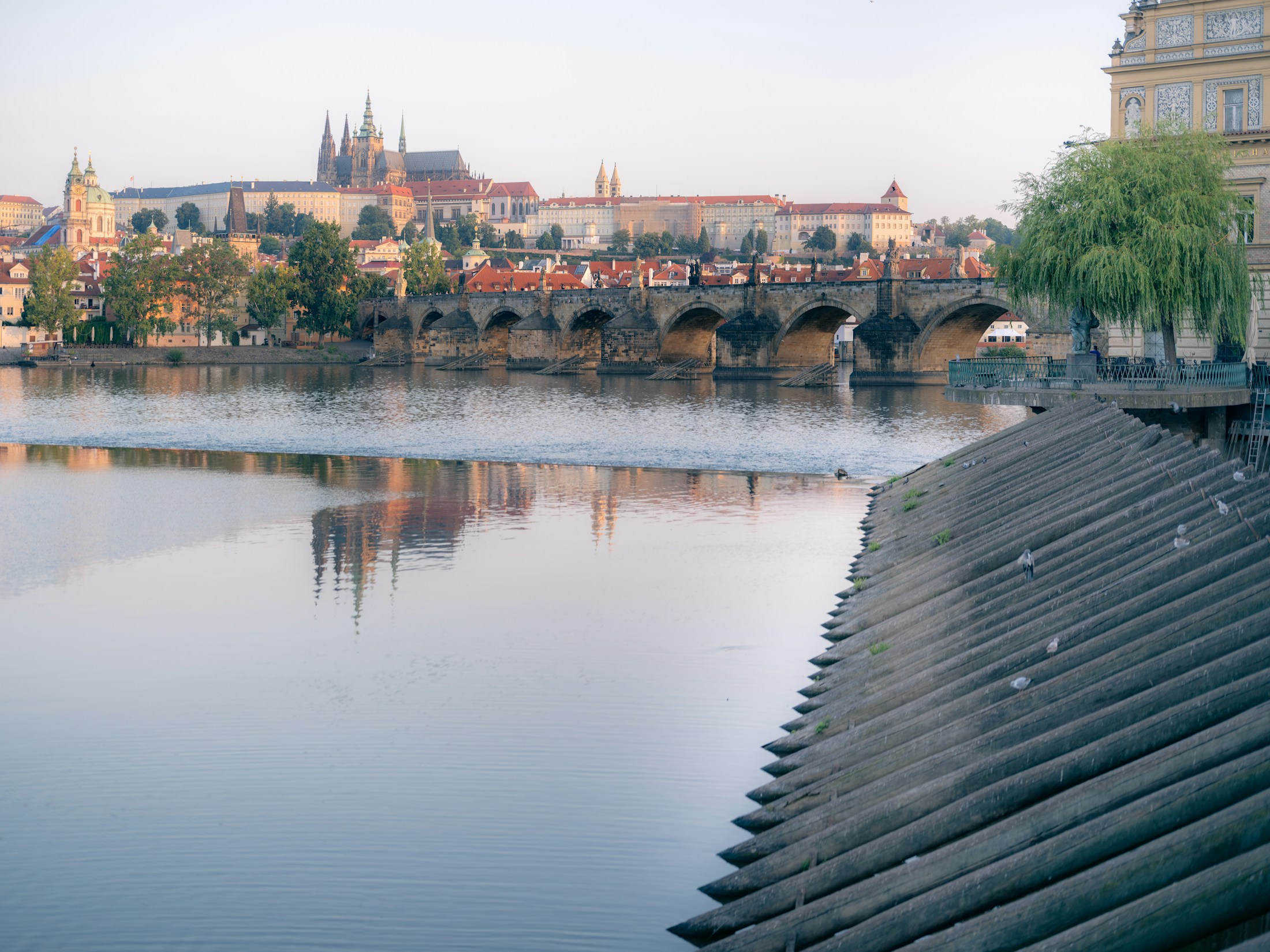 Karlův most a Pražský hrad nad klidnou Vltavou za svítání